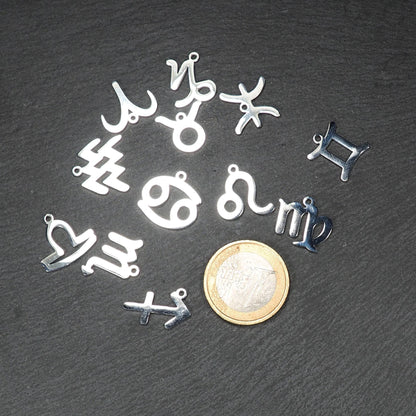 Mehrere flache silberne Sternzeichen-Anhänger aus glänzendem Metall mit Öse, neben Ein-Euro-Münze als Größenvergleich.