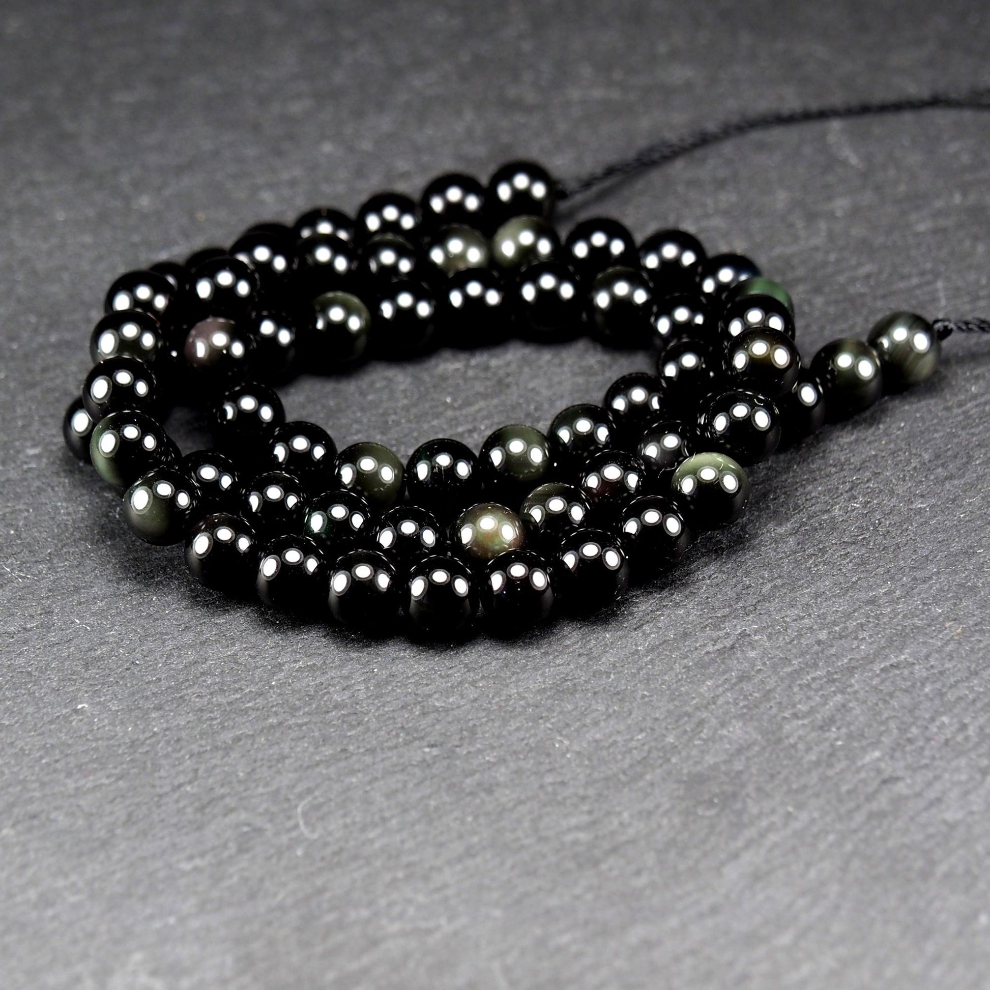 Aufgereihter Perlenstrang aus tiefschwarzen, hochglänzend-polierten, kugelförmigen Obsidianperlen mit glatter Oberfläche.