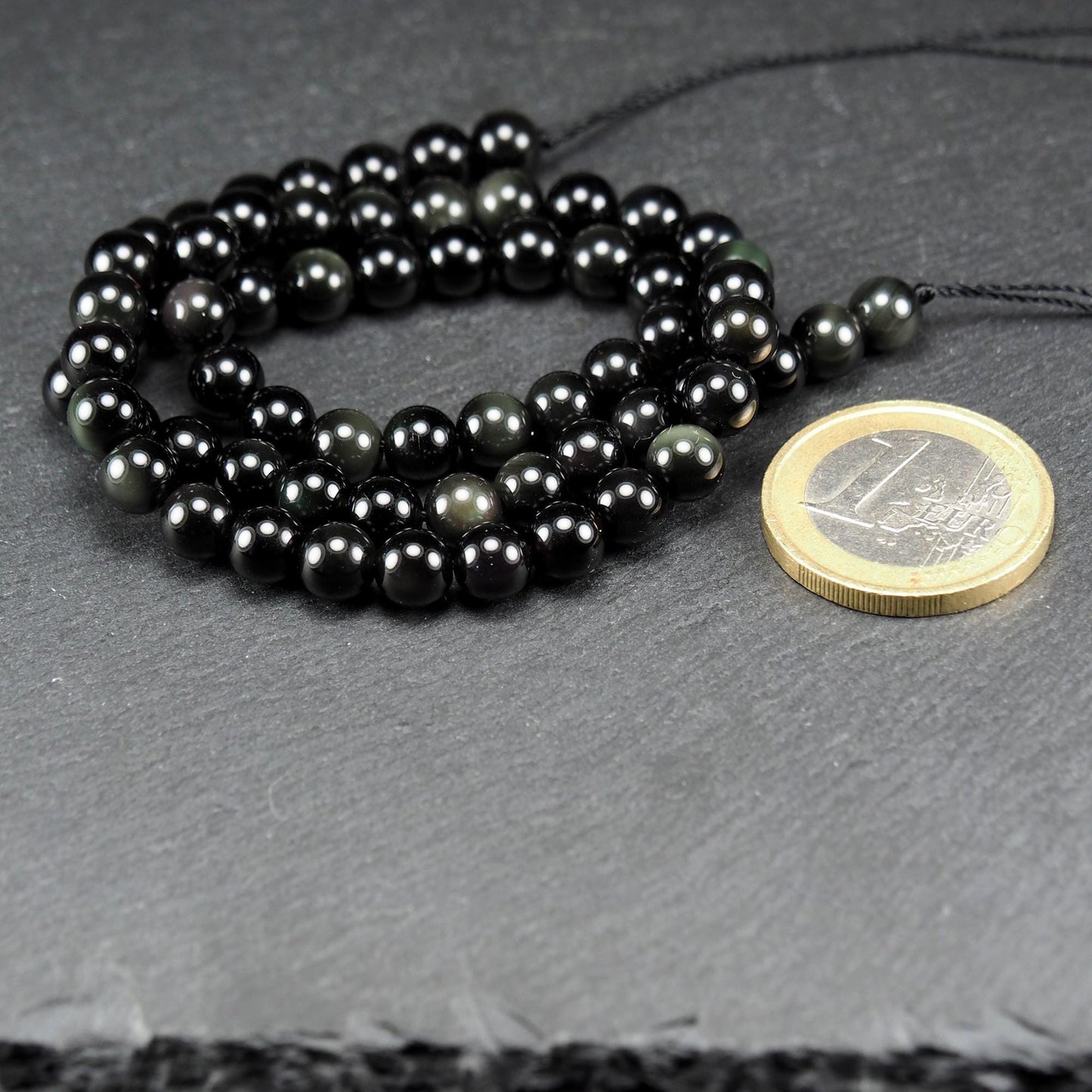 Aufgereihter Perlenstrang aus tiefschwarzen, hochglänzend-polierten, kugelförmigen Obsidianperlen mit glatter Oberfläche.