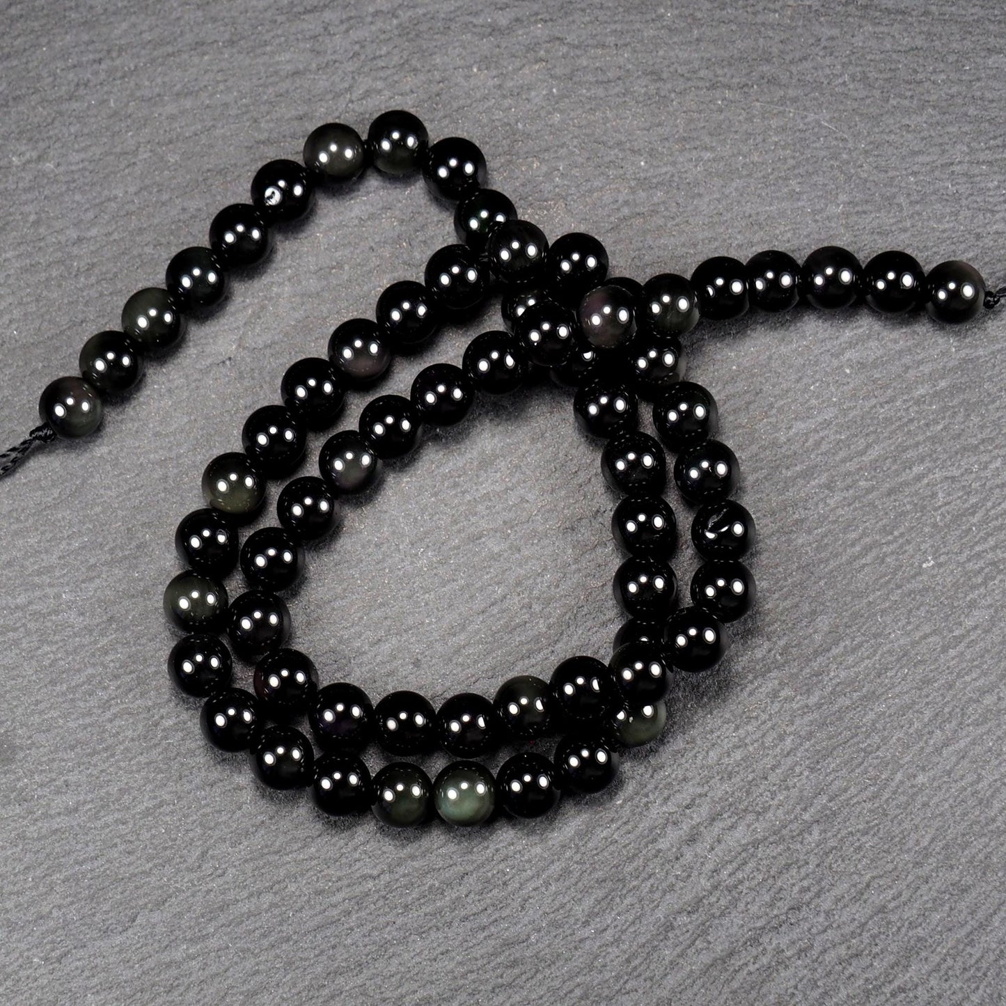 Aufgereihter Perlenstrang aus tiefschwarzen, hochglänzend-polierten, kugelförmigen Obsidianperlen mit glatter Oberfläche.