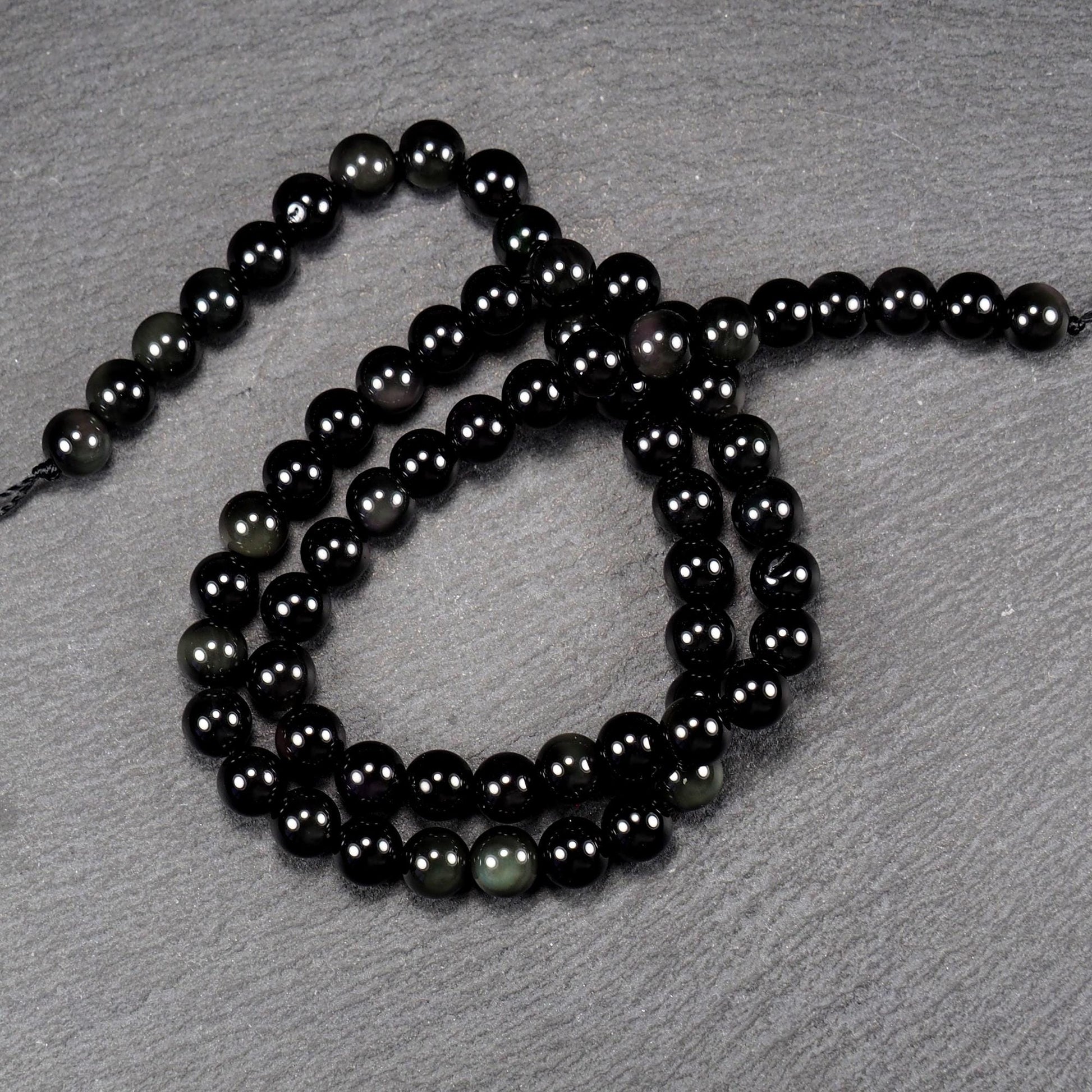 Aufgereihter Perlenstrang aus tiefschwarzen, hochglänzend-polierten, kugelförmigen Obsidianperlen mit glatter Oberfläche.