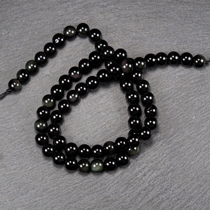 Aufgereihter Perlenstrang aus tiefschwarzen, hochglänzend-polierten, kugelförmigen Obsidianperlen mit glatter Oberfläche.