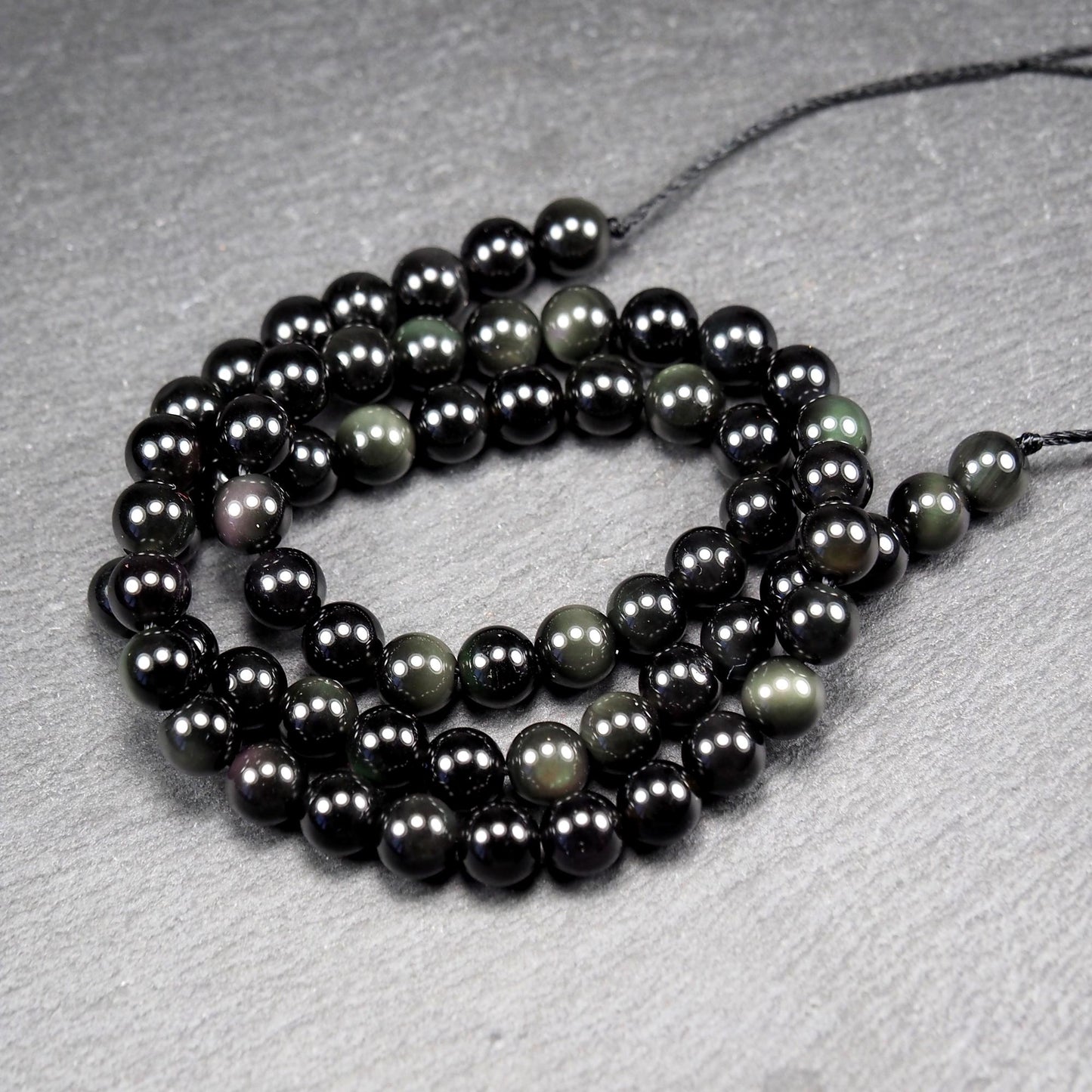 Aufgereihter Perlenstrang aus tiefschwarzen, hochglänzend-polierten, kugelförmigen Obsidianperlen mit glatter Oberfläche.