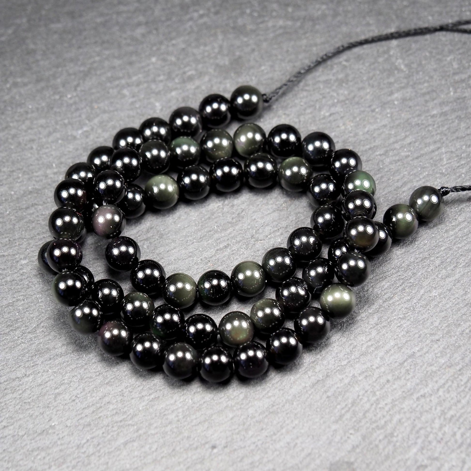 Aufgereihter Perlenstrang aus tiefschwarzen, hochglänzend-polierten, kugelförmigen Obsidianperlen mit glatter Oberfläche.
