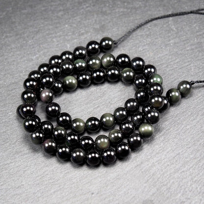 Aufgereihter Perlenstrang aus tiefschwarzen, hochglänzend-polierten, kugelförmigen Obsidianperlen mit glatter Oberfläche.