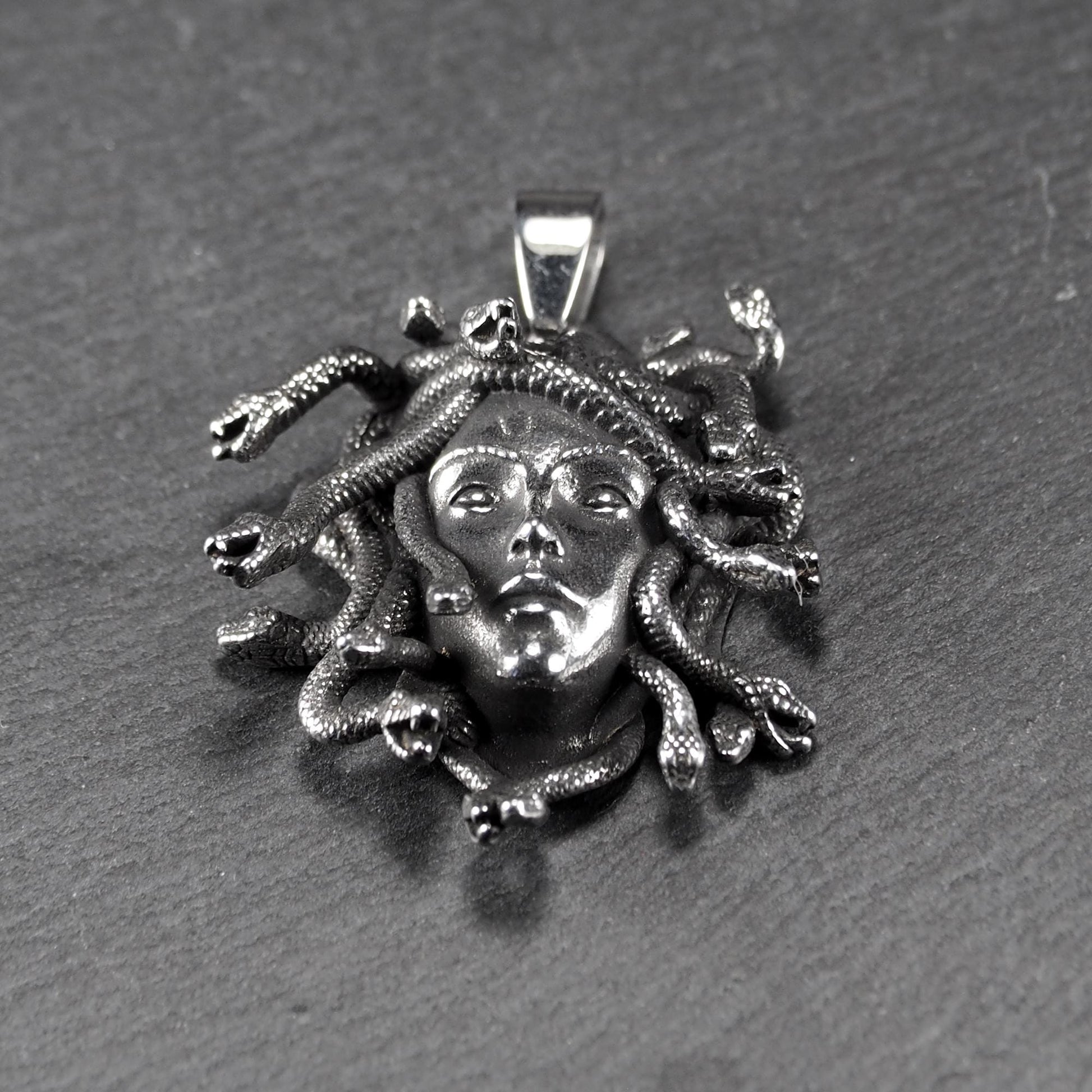 Silberfarbener, dreidimensionaler und glänzender Medusa-Anhänger in Relief mit menschlichem Gesicht und vielen schlangenförmigen Haaren, sichtbarer Öse.