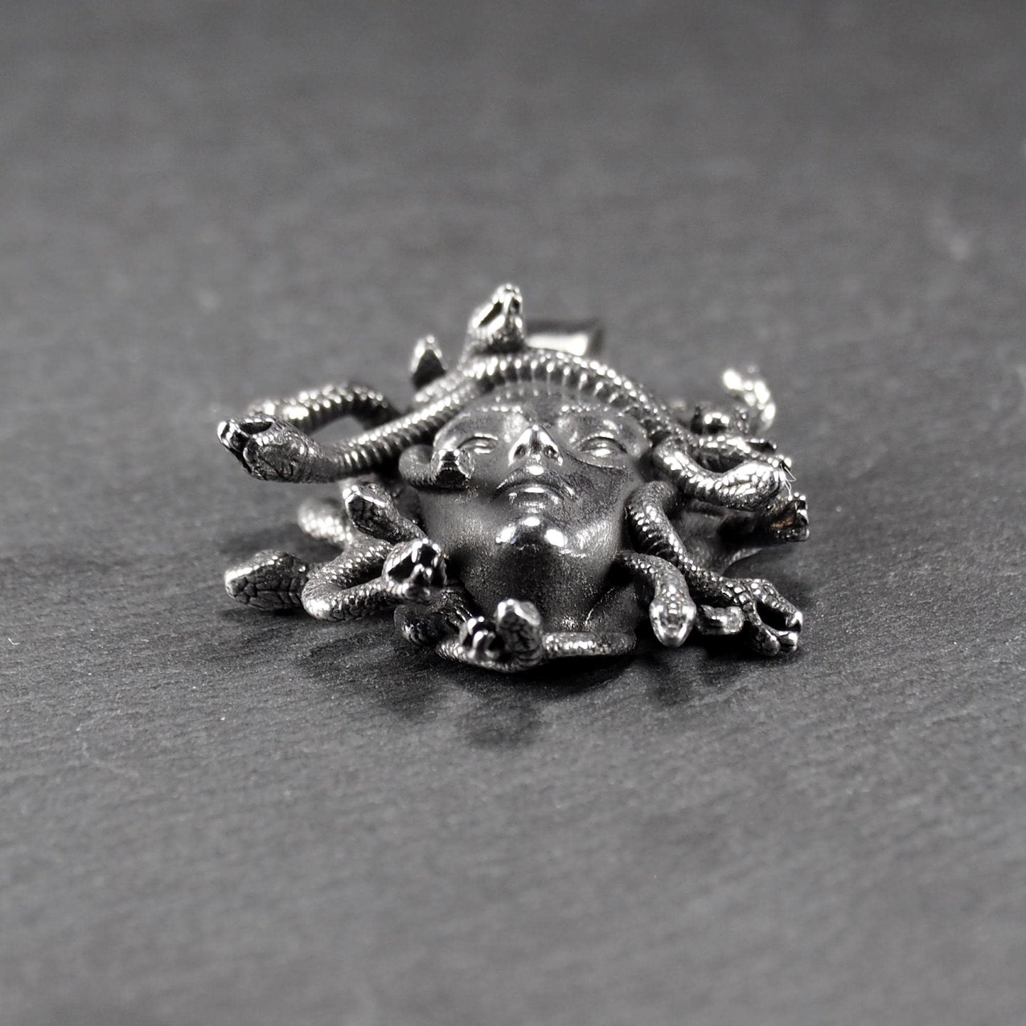 Silberfarbener, dreidimensionaler und glänzender Medusa-Anhänger in Relief mit menschlichem Gesicht und vielen schlangenförmigen Haaren, sichtbarer Öse.