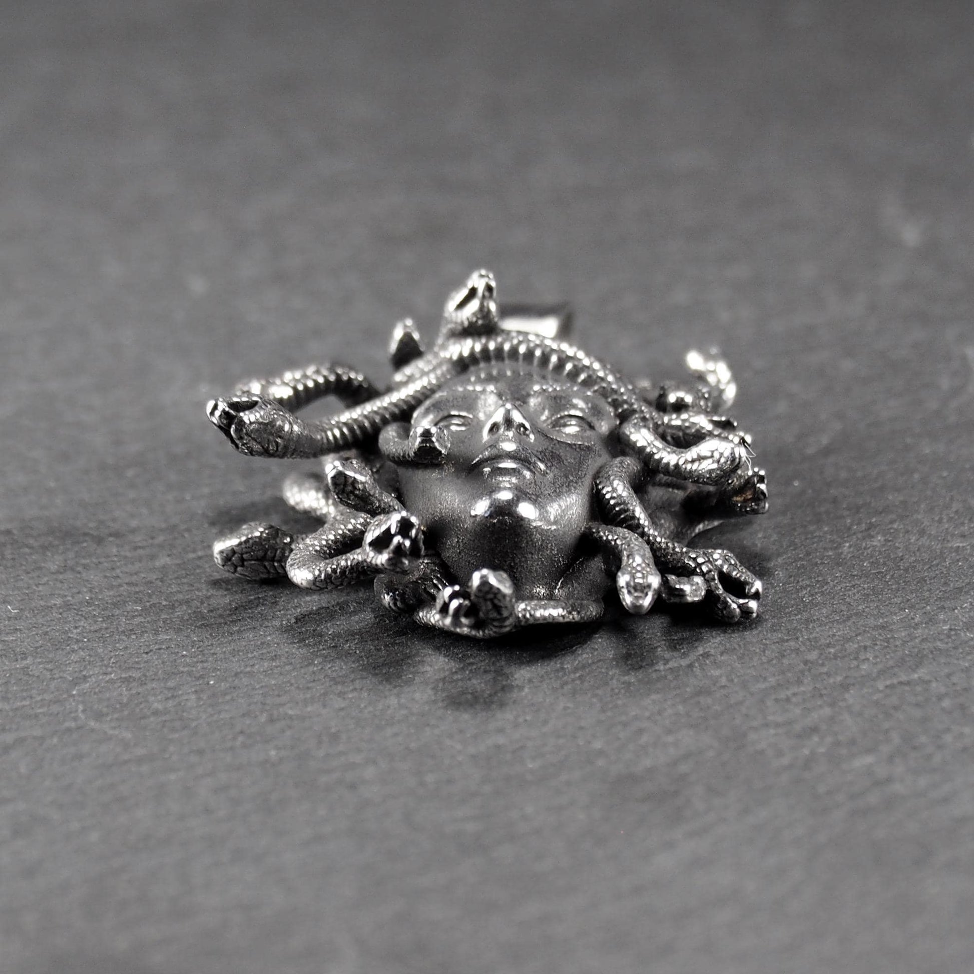 Silberfarbener, dreidimensionaler und glänzender Medusa-Anhänger in Relief mit menschlichem Gesicht und vielen schlangenförmigen Haaren, sichtbarer Öse.