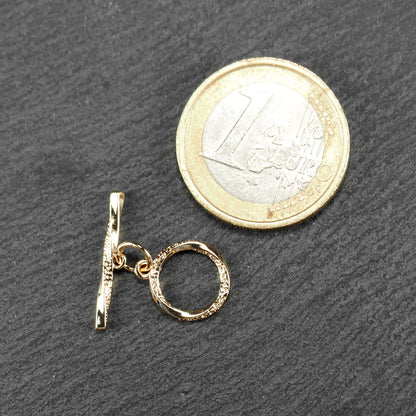 Knebelverschluss, goldfarben, mit runder durchbrochener Öse mit punktierter Struktur und horizontalem Stab, verbunden durch kleine Ringe.