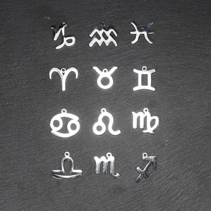 Zwölf flache silberfarbene Edelstahl-Anhänger als durchbrochene Sternzeichensymbole mit glänzender Oberfläche und je einer Öse auf dunklem Hintergrund.