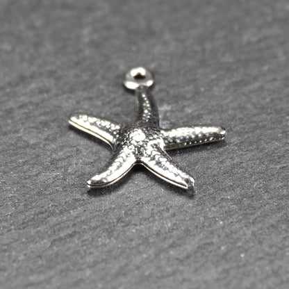 Seestern-Anhänger aus silberfarbenem Metall mit reliefartiger, strukturierter glänzender Oberfläche, fünf Armen und kleiner runder Öse oben.