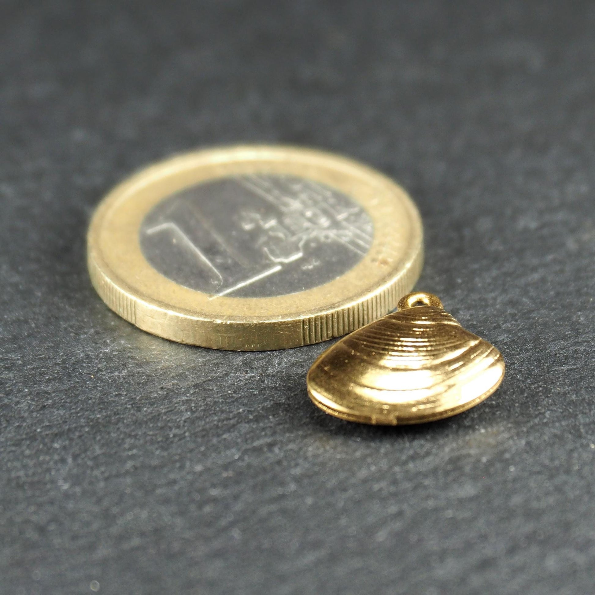 Kleiner muschelförmiger Anhänger, goldfarbene glänzende Oberfläche mit konzentrischen Rillen und integrierter Öse oben.