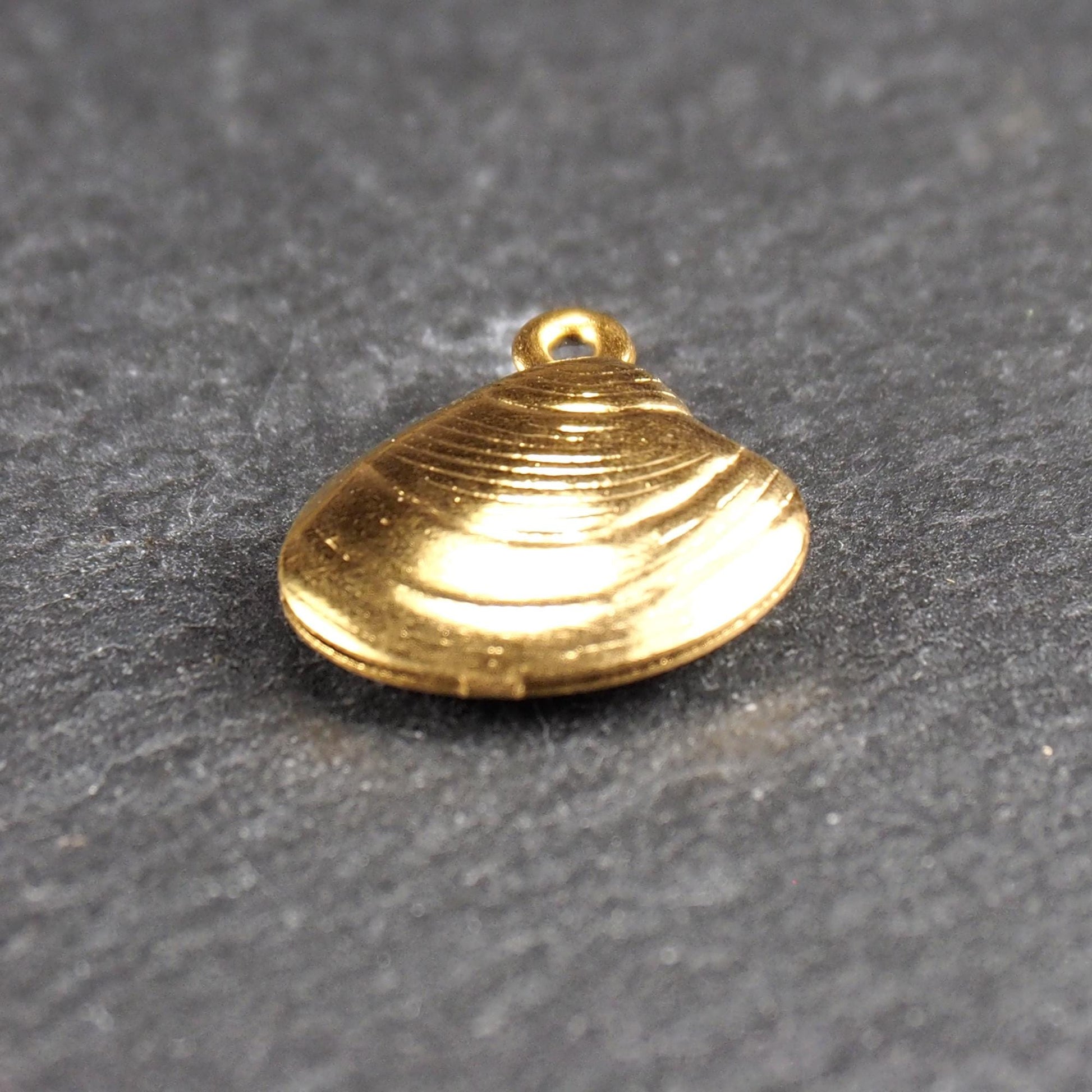 Kleiner muschelförmiger Anhänger, goldfarbene glänzende Oberfläche mit konzentrischen Rillen und integrierter Öse oben.
