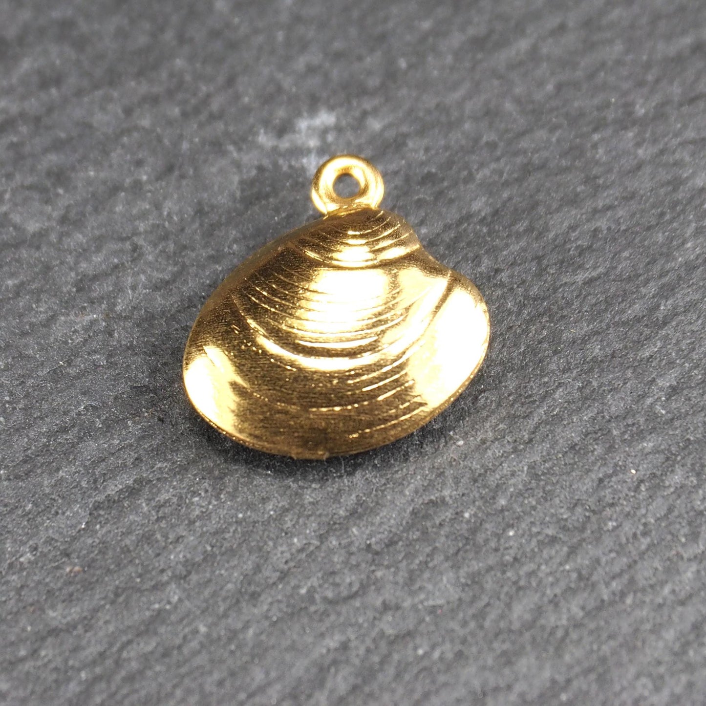 Kleiner muschelförmiger Anhänger, goldfarbene glänzende Oberfläche mit konzentrischen Rillen und integrierter Öse oben.