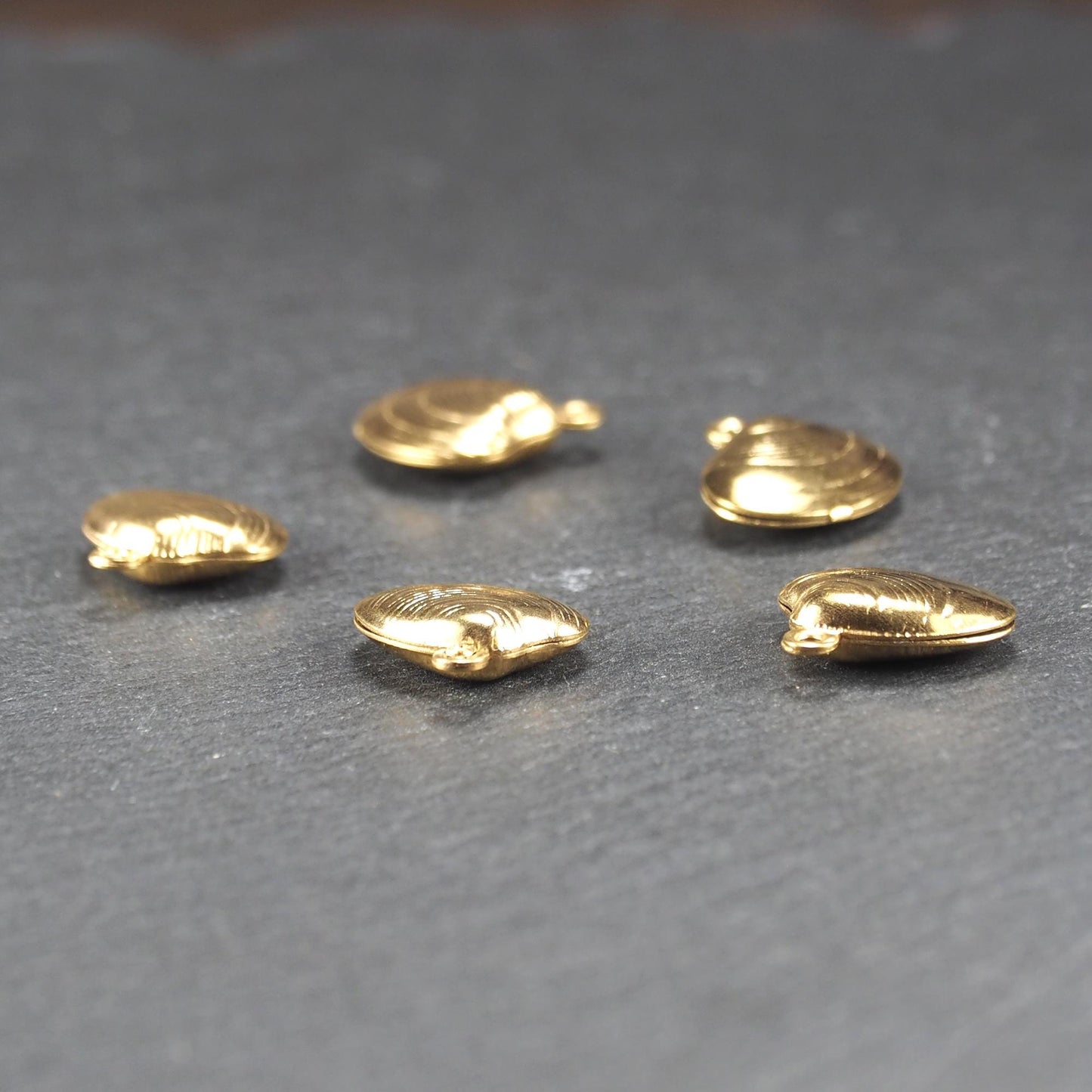 Kleiner muschelförmiger Anhänger, goldfarbene glänzende Oberfläche mit konzentrischen Rillen und integrierter Öse oben.