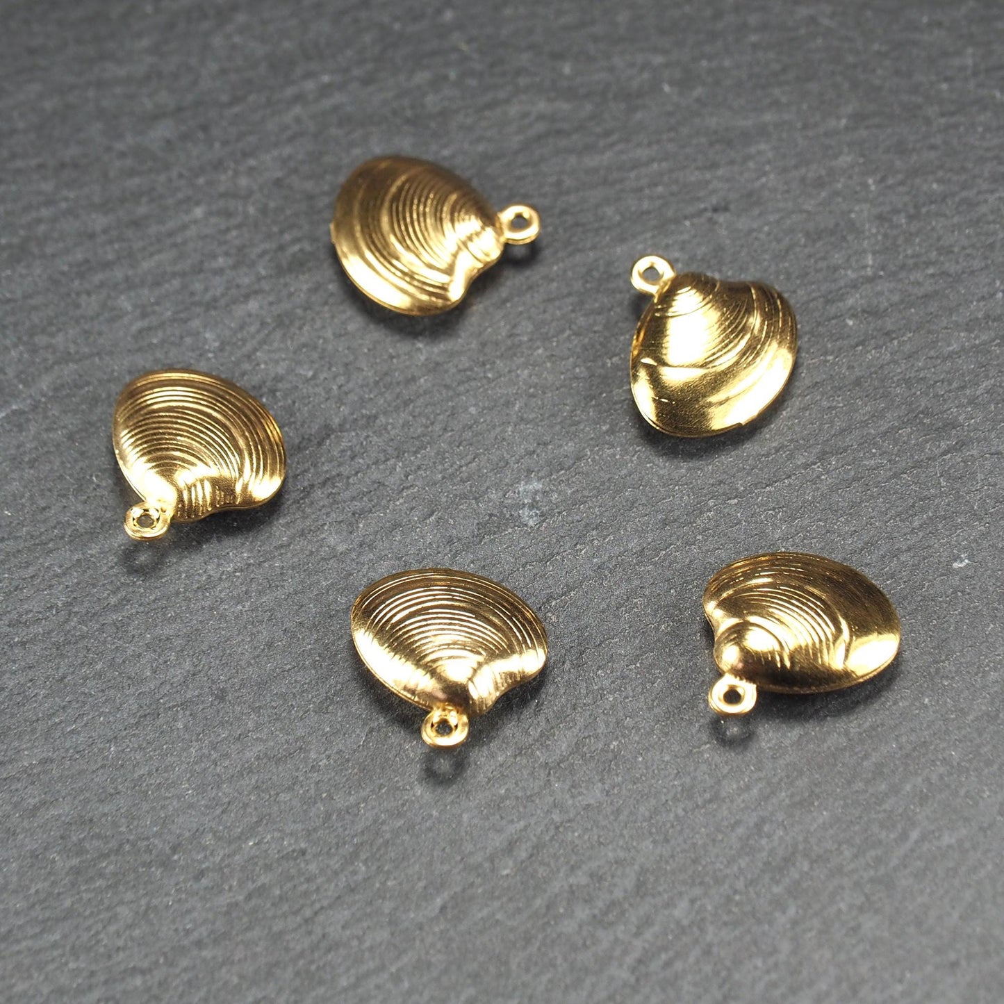Kleiner muschelförmiger Anhänger, goldfarbene glänzende Oberfläche mit konzentrischen Rillen und integrierter Öse oben.