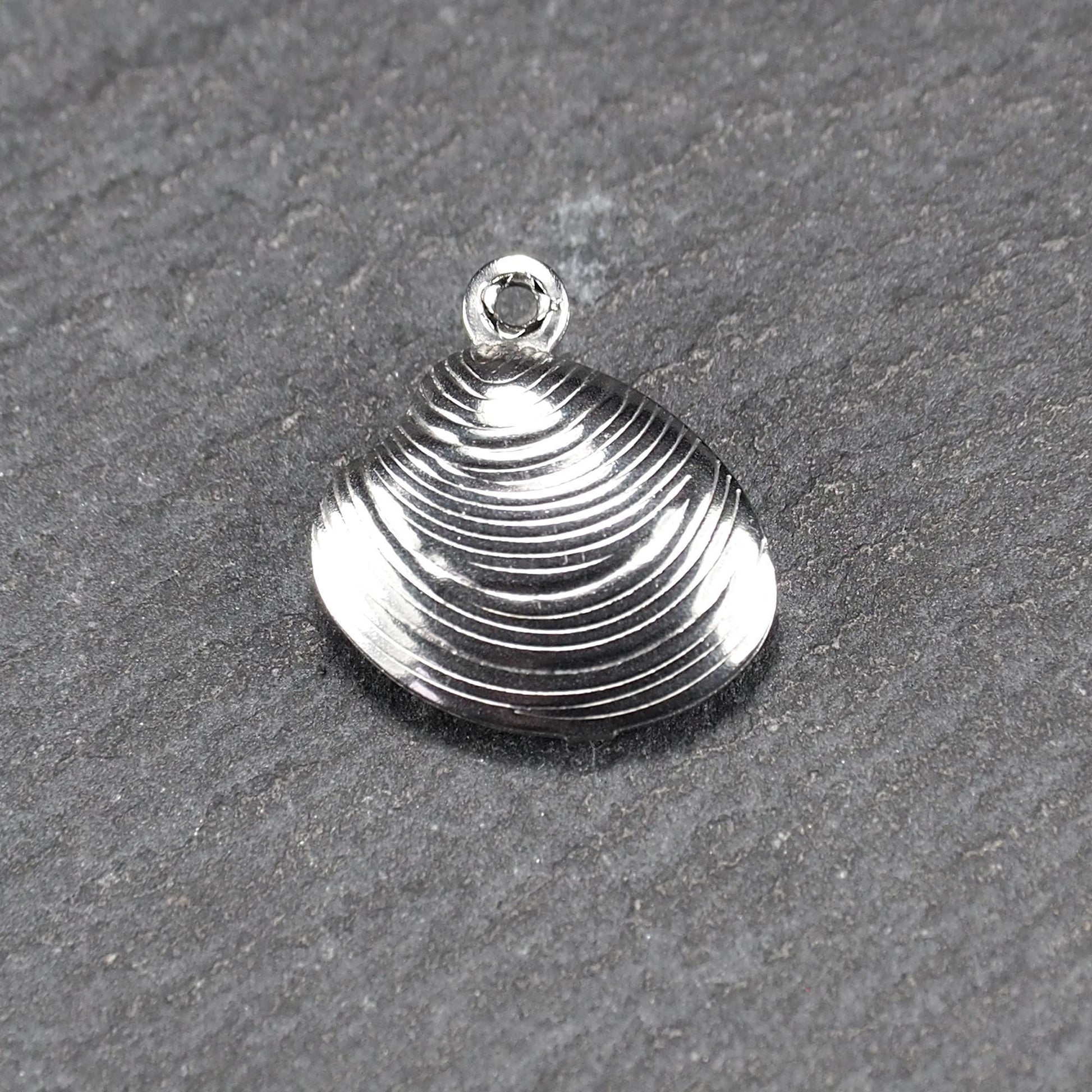 Muschelförmiger silberfarbener Anhänger mit polierter, glänzender Oberfläche, konzentrisch geriffelten Rillen und integrierter runder Öse oben.