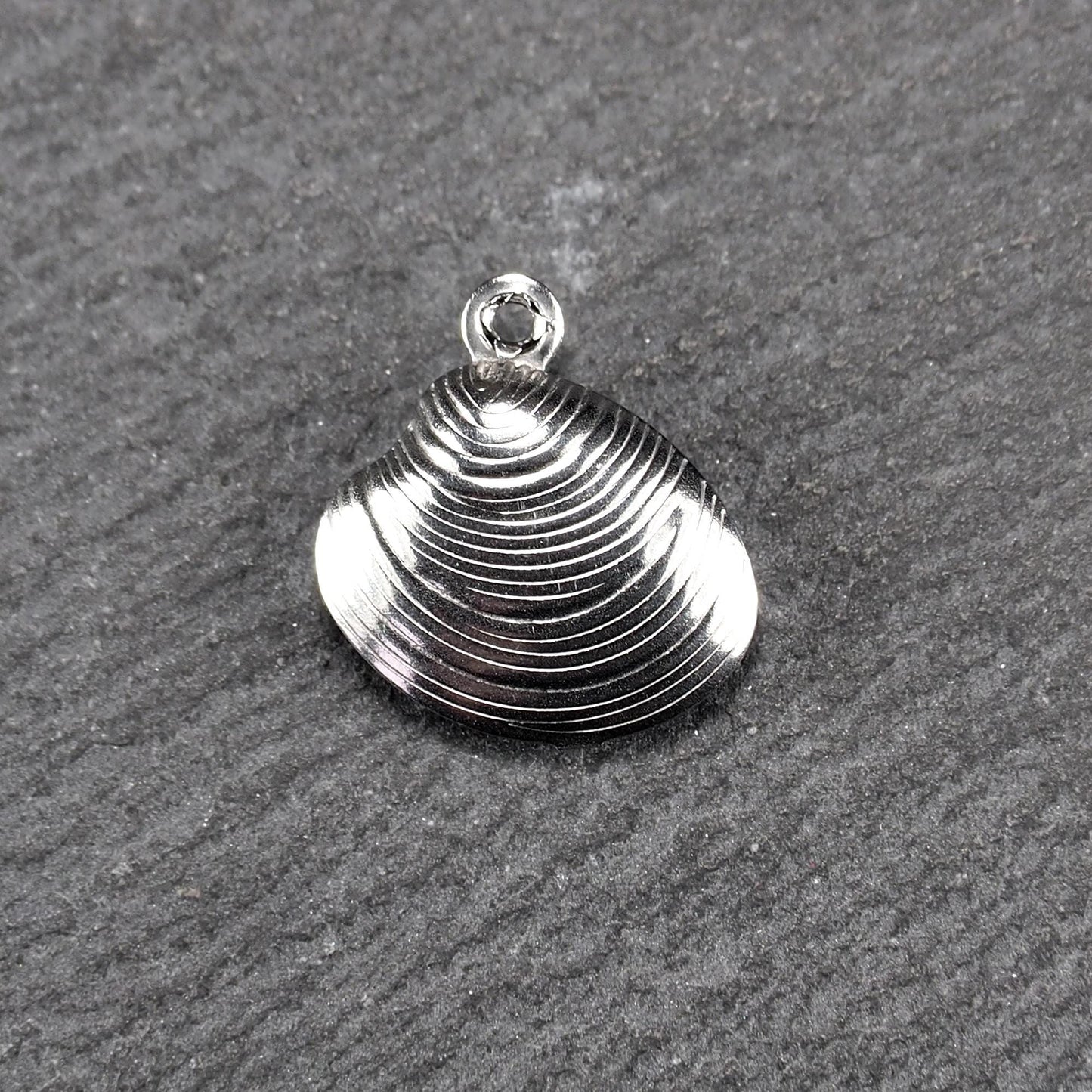 Muschelförmiger silberfarbener Anhänger mit polierter, glänzender Oberfläche, konzentrisch geriffelten Rillen und integrierter runder Öse oben.