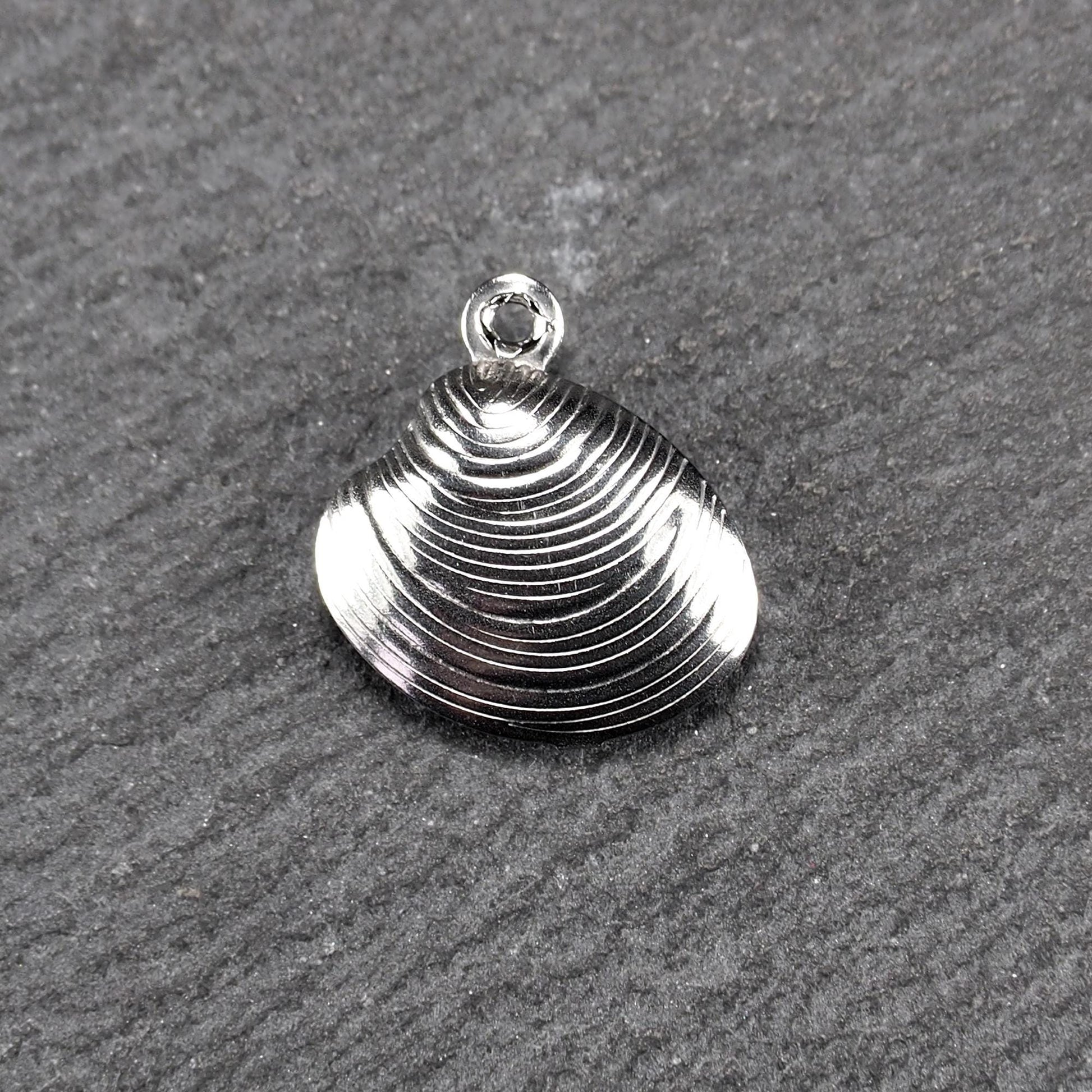 Muschelförmiger silberfarbener Anhänger mit polierter, glänzender Oberfläche, konzentrisch geriffelten Rillen und integrierter runder Öse oben.