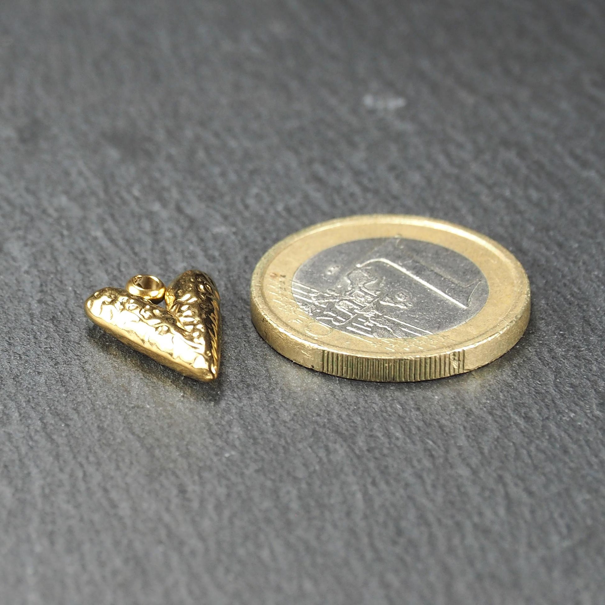 Herzförmiger goldfarbener Anhänger mit reliefierter, glänzender Oberfläche, integrierter Öse oben, neben einer 1‑Euro‑Münze.