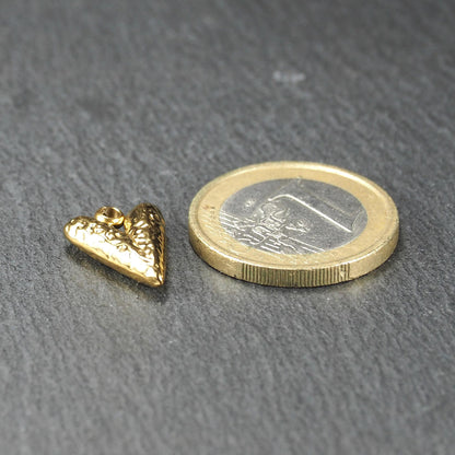 Herzförmiger goldfarbener Anhänger mit reliefierter, glänzender Oberfläche, integrierter Öse oben, neben einer 1‑Euro‑Münze.