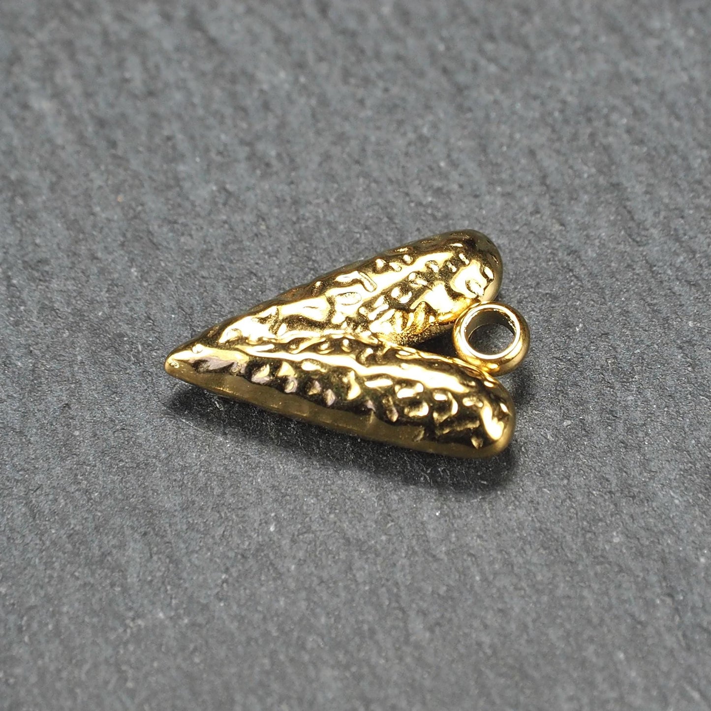 Herzförmiger, vergoldeter Anhänger mit strukturierter Reliefoberfläche, spitz zulaufender Form und integrierter Öse oben.