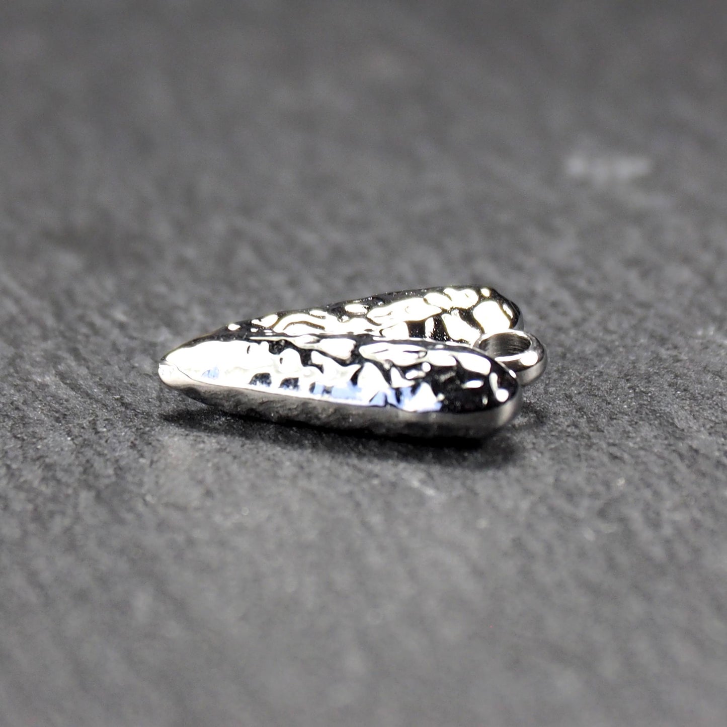 Herzanhänger, silberfarbig hochglänzend mit reliefartiger Oberfläche, spitz zulaufender Unterseite und integrierter runder Öse.