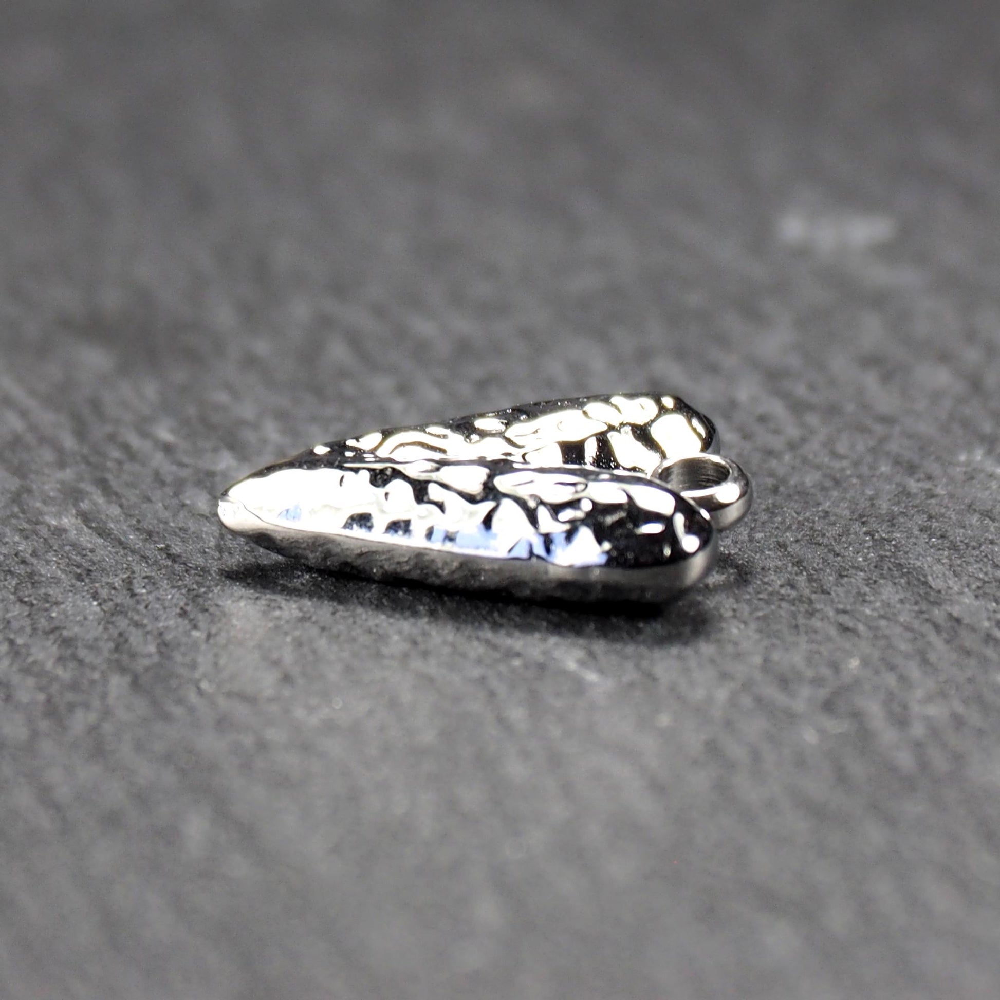 Herzanhänger, silberfarbig hochglänzend mit reliefartiger Oberfläche, spitz zulaufender Unterseite und integrierter runder Öse.