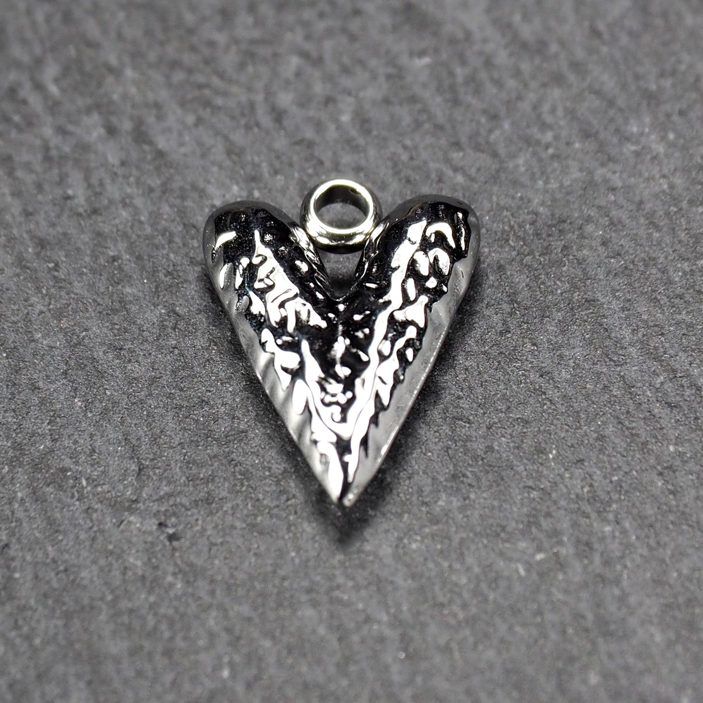 Herzanhänger, silberfarbig hochglänzend mit reliefartiger Oberfläche, spitz zulaufender Unterseite und integrierter runder Öse.