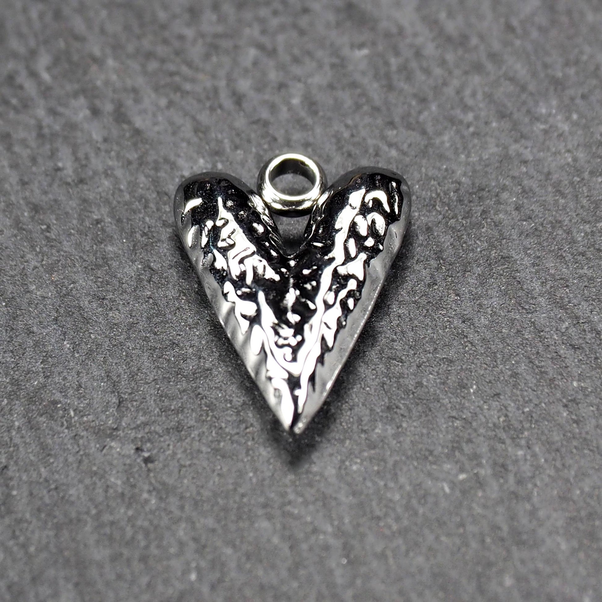 Herzanhänger, silberfarbig hochglänzend mit reliefartiger Oberfläche, spitz zulaufender Unterseite und integrierter runder Öse.