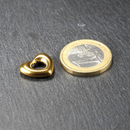 Herzförmiger, goldglänzender Anhänger mit offenem, durchbrochenem Zentrum und rundem Fädelloch, daneben 1-Euro-Münze als Größenvergleich.