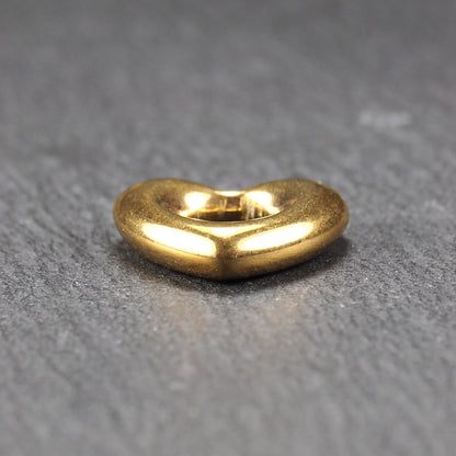 Herzförmiger, goldfarbener Anhänger mit hochglänzender, glatter Oberfläche, rundem durchbrochenem Zentrum und sichtbarer Bohrung.