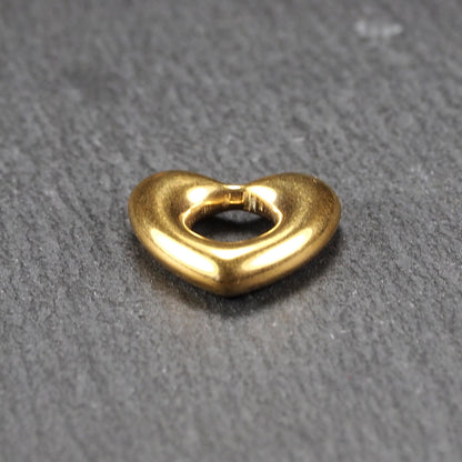 Herzförmiger, goldfarbener Anhänger mit hochglänzender, glatter Oberfläche, rundem durchbrochenem Zentrum und sichtbarer Bohrung.