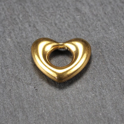 Herzförmiger, goldfarbener Anhänger mit hochglänzender, glatter Oberfläche, rundem durchbrochenem Zentrum und sichtbarer Bohrung.