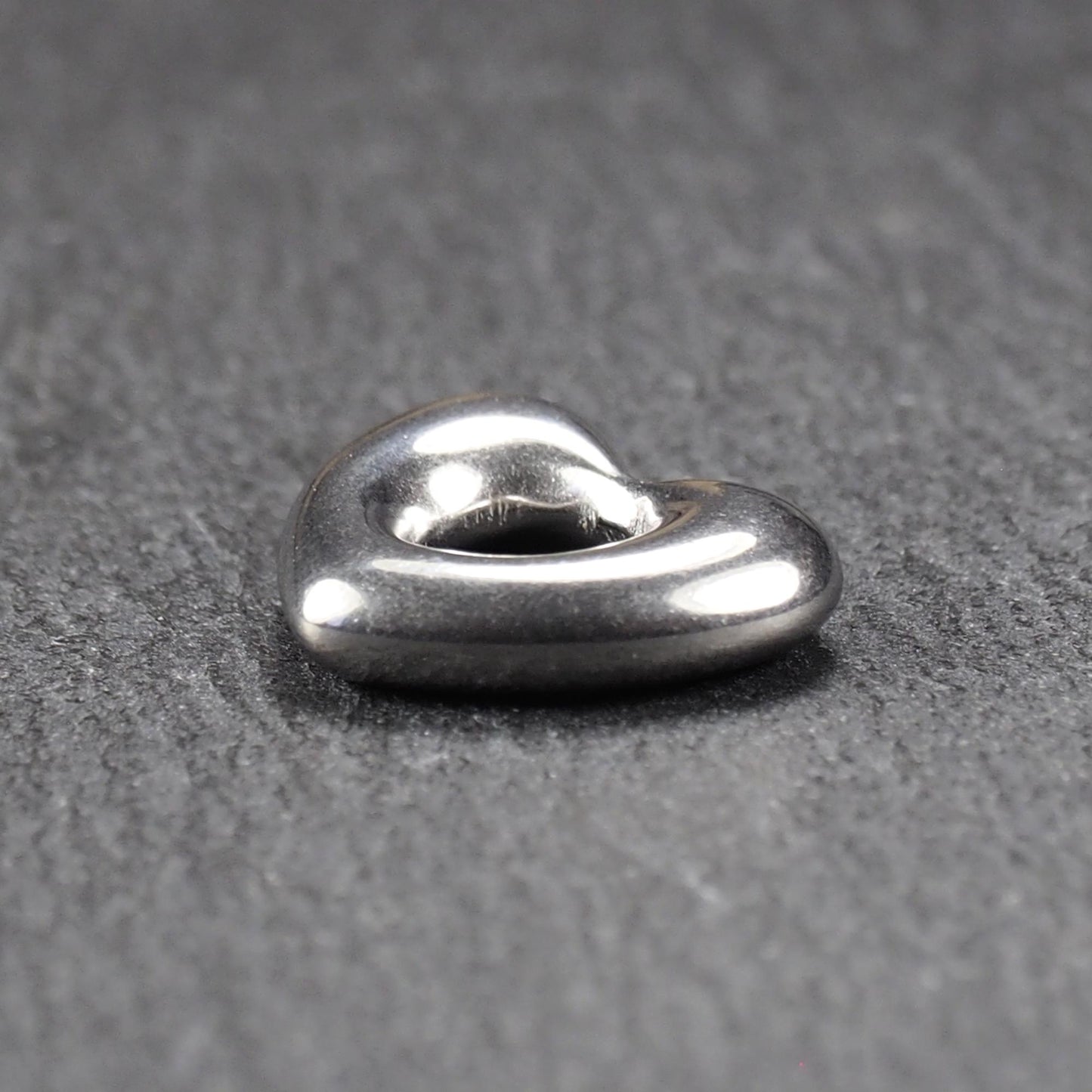Herzanhänger, glänzend poliertes silbernes Metall mit rundem, durchbrochenem Innenfeld und glatten, abgerundeten Kanten auf dunklem Hintergrund.