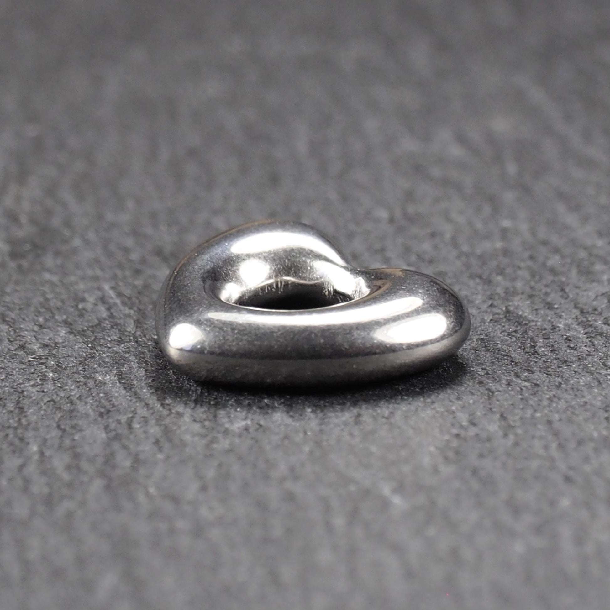 Herzanhänger, glänzend poliertes silbernes Metall mit rundem, durchbrochenem Innenfeld und glatten, abgerundeten Kanten auf dunklem Hintergrund.