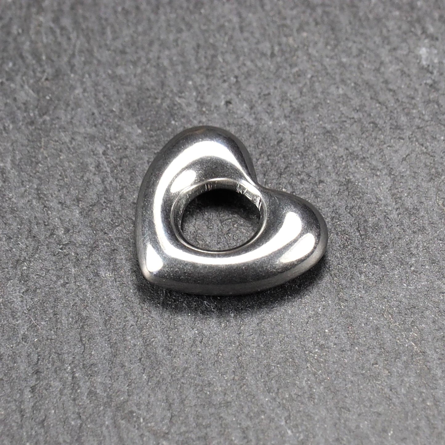 Herzanhänger, glänzend poliertes silbernes Metall mit rundem, durchbrochenem Innenfeld und glatten, abgerundeten Kanten auf dunklem Hintergrund.