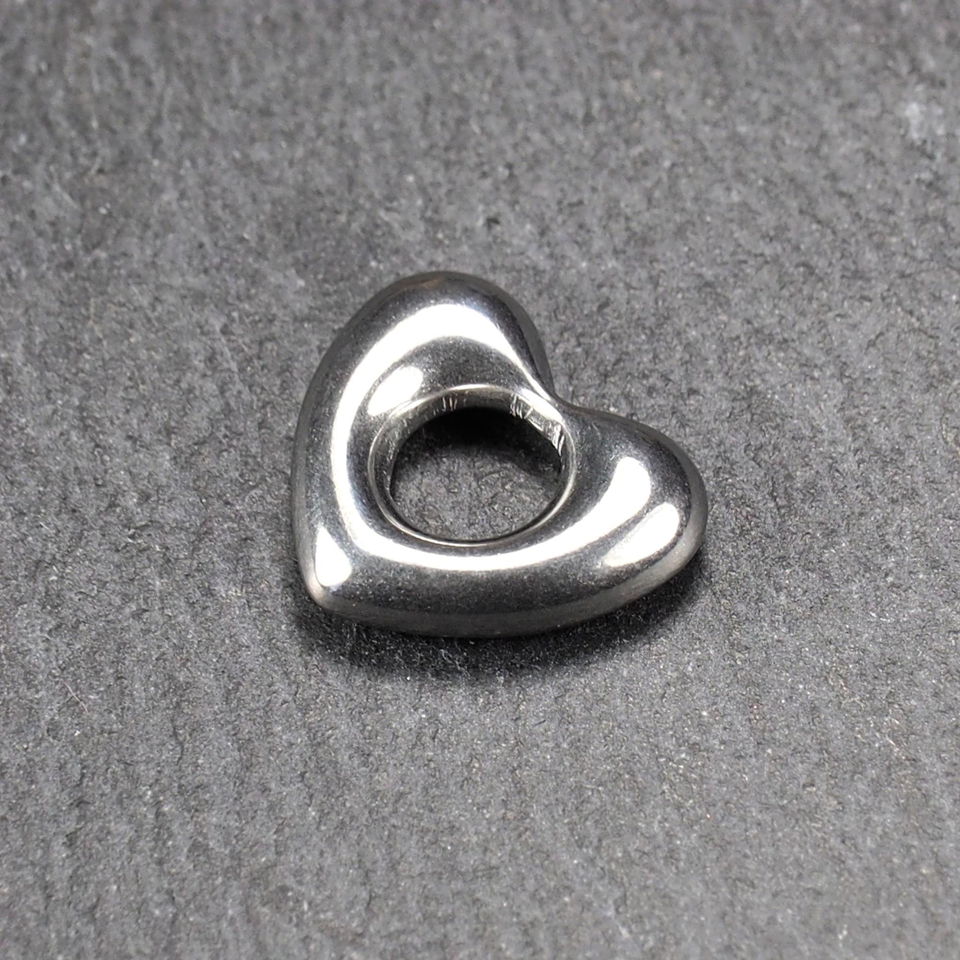 Herzanhänger, glänzend poliertes silbernes Metall mit rundem, durchbrochenem Innenfeld und glatten, abgerundeten Kanten auf dunklem Hintergrund.