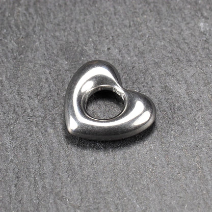 Herzanhänger, glänzend poliertes silbernes Metall mit rundem, durchbrochenem Innenfeld und glatten, abgerundeten Kanten auf dunklem Hintergrund.