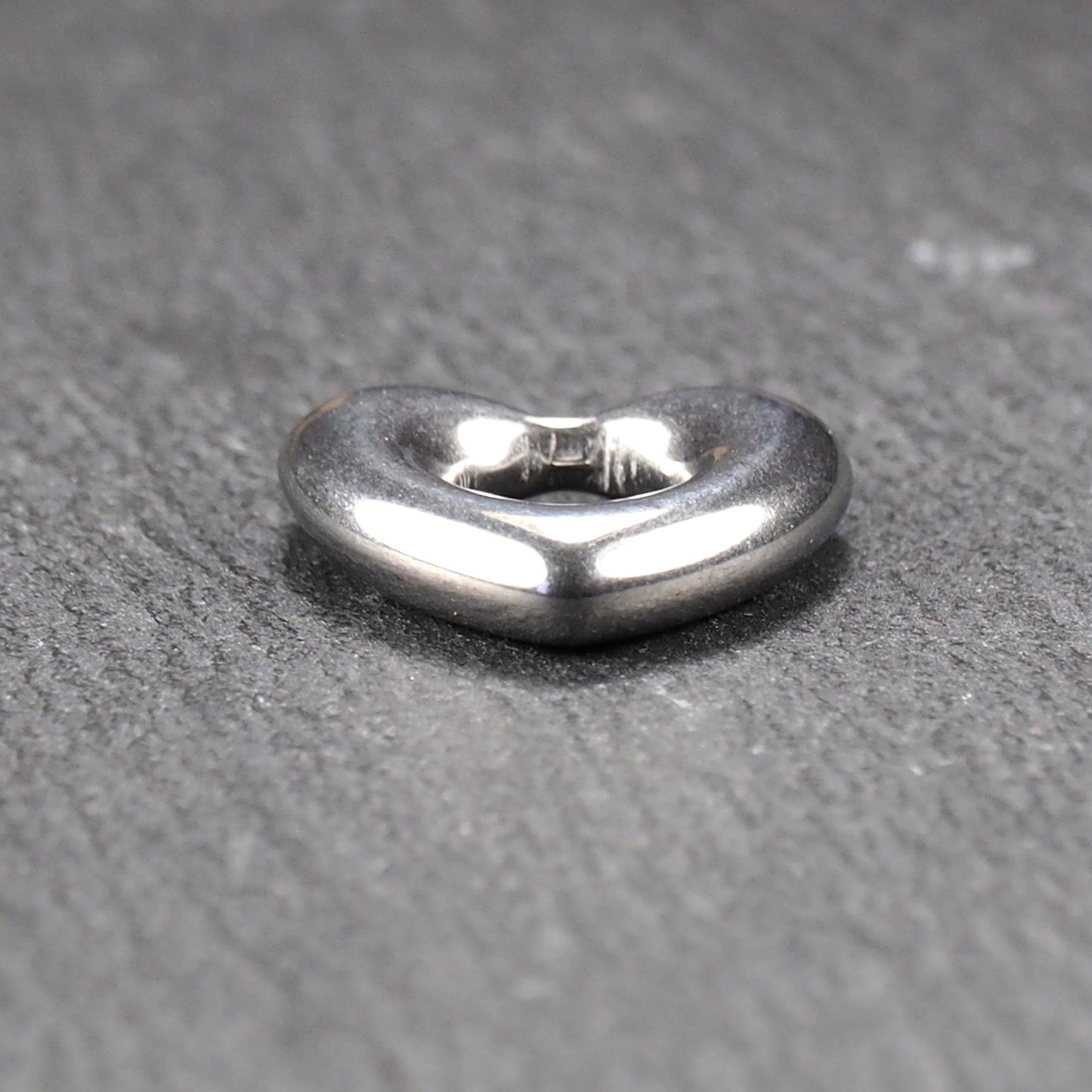 Herzanhänger, glänzend poliertes silbernes Metall mit rundem, durchbrochenem Innenfeld und glatten, abgerundeten Kanten auf dunklem Hintergrund.