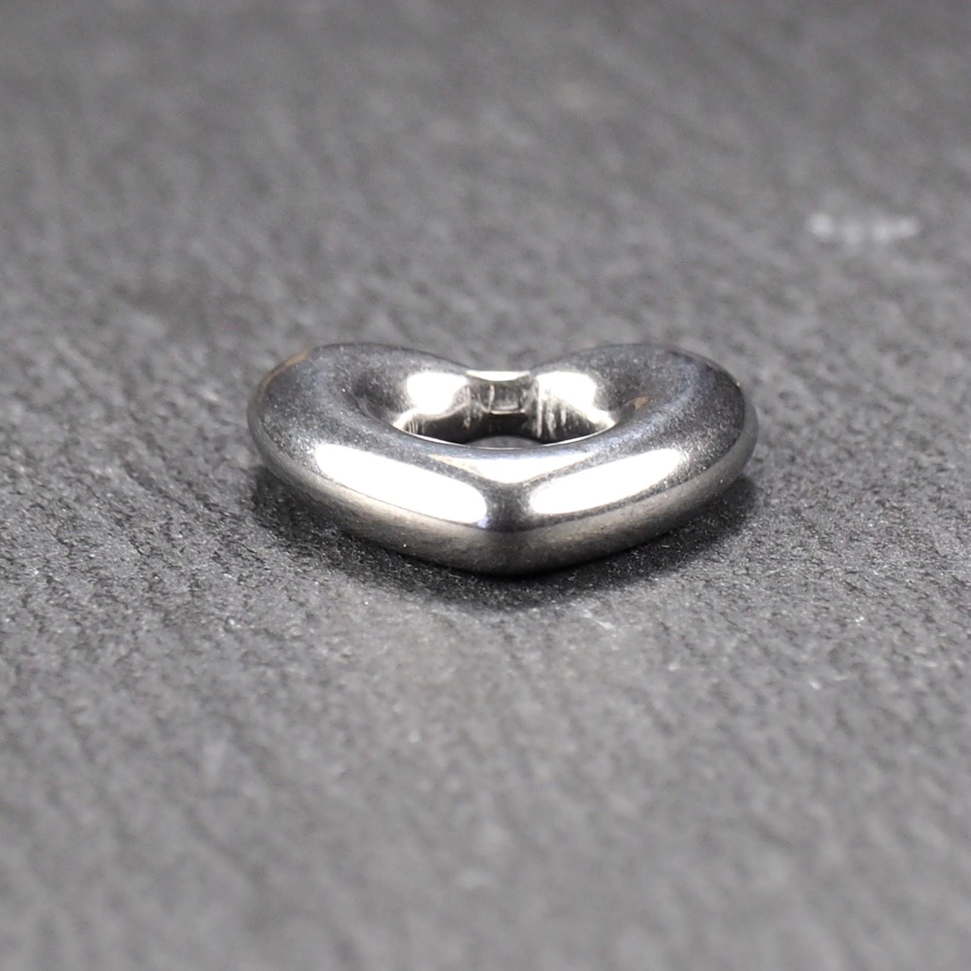 Herzanhänger, glänzend poliertes silbernes Metall mit rundem, durchbrochenem Innenfeld und glatten, abgerundeten Kanten auf dunklem Hintergrund.