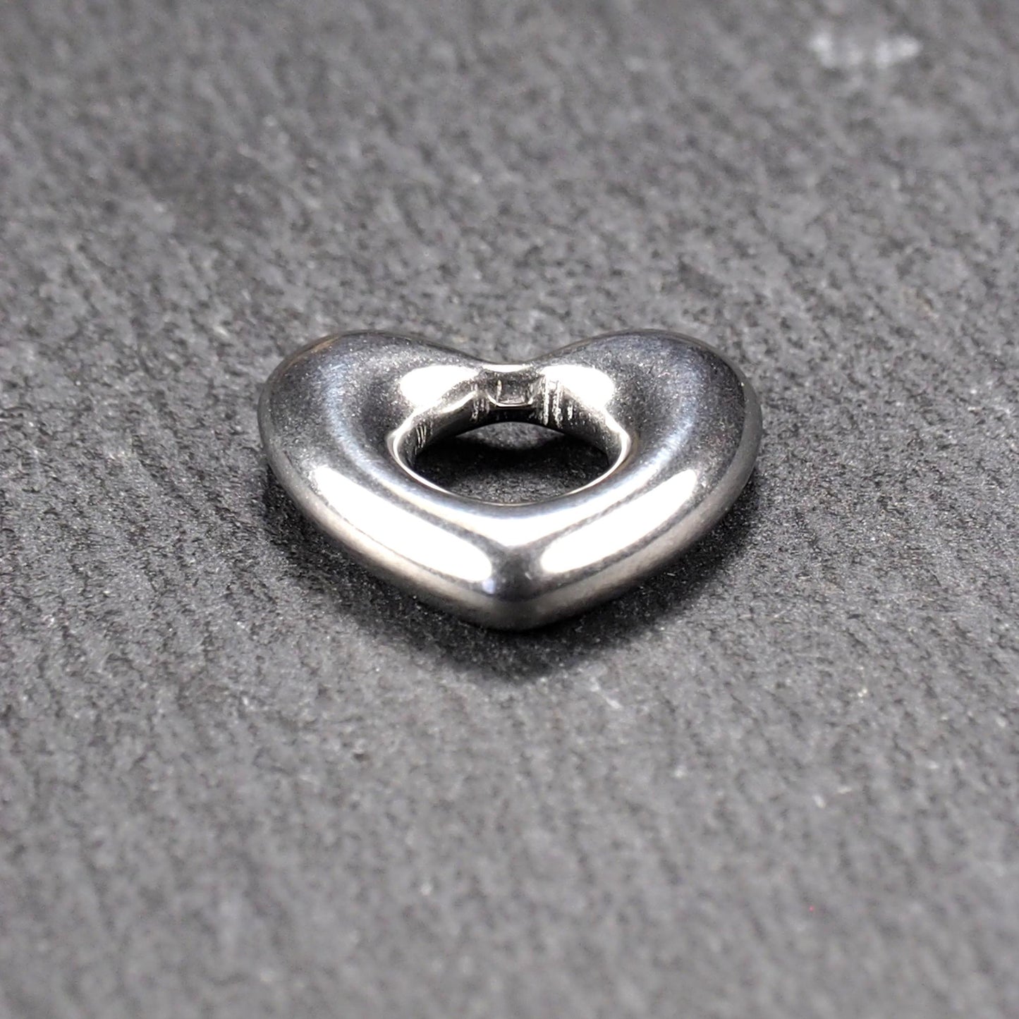 Herzanhänger, glänzend poliertes silbernes Metall mit rundem, durchbrochenem Innenfeld und glatten, abgerundeten Kanten auf dunklem Hintergrund.