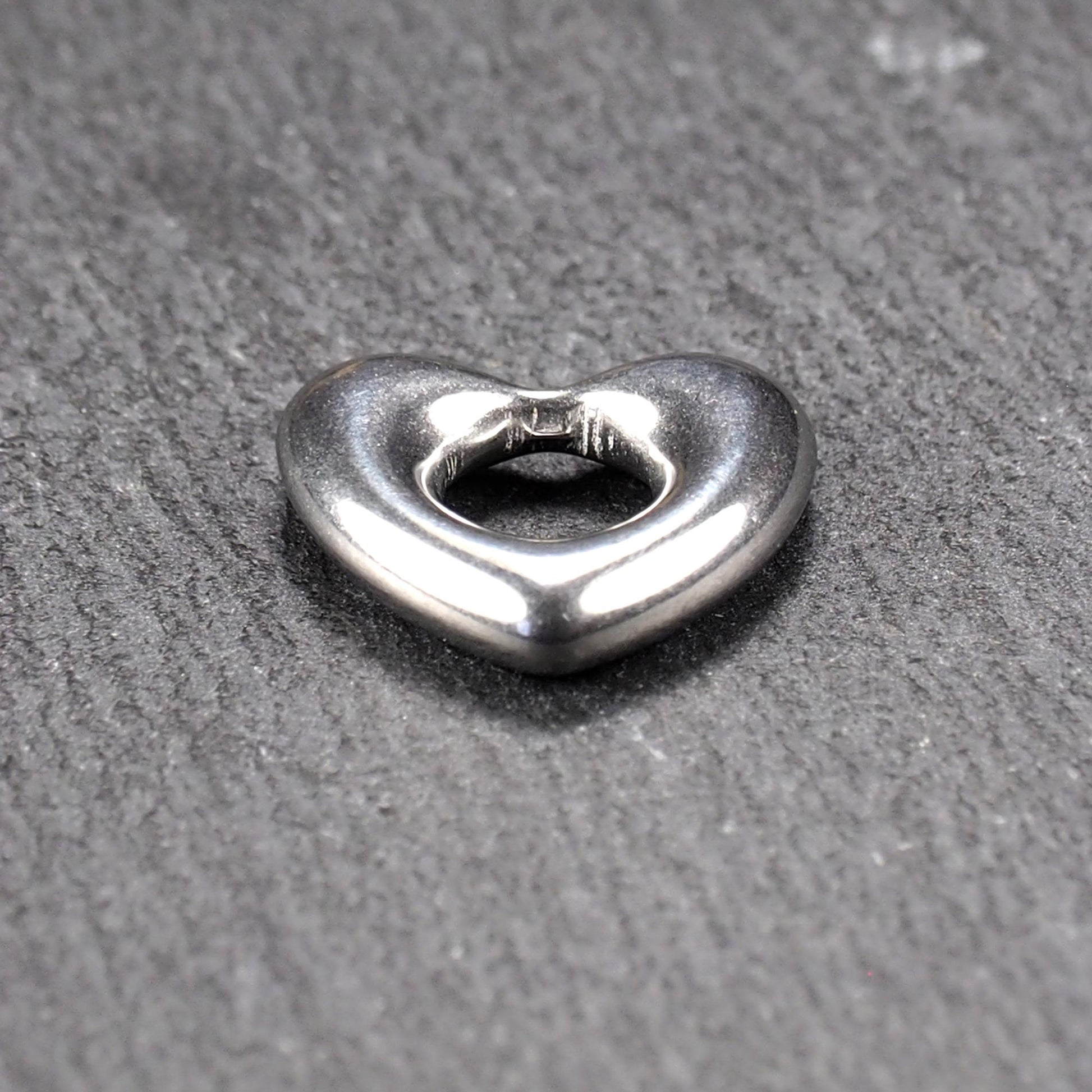 Herzanhänger, glänzend poliertes silbernes Metall mit rundem, durchbrochenem Innenfeld und glatten, abgerundeten Kanten auf dunklem Hintergrund.