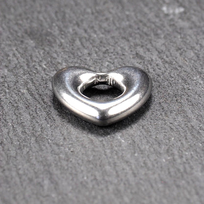 Herzanhänger, glänzend poliertes silbernes Metall mit rundem, durchbrochenem Innenfeld und glatten, abgerundeten Kanten auf dunklem Hintergrund.