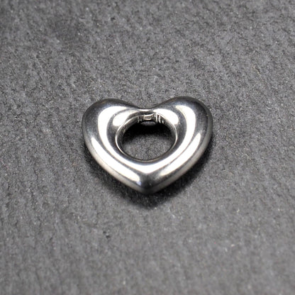 Herzanhänger, glänzend poliertes silbernes Metall mit rundem, durchbrochenem Innenfeld und glatten, abgerundeten Kanten auf dunklem Hintergrund.
