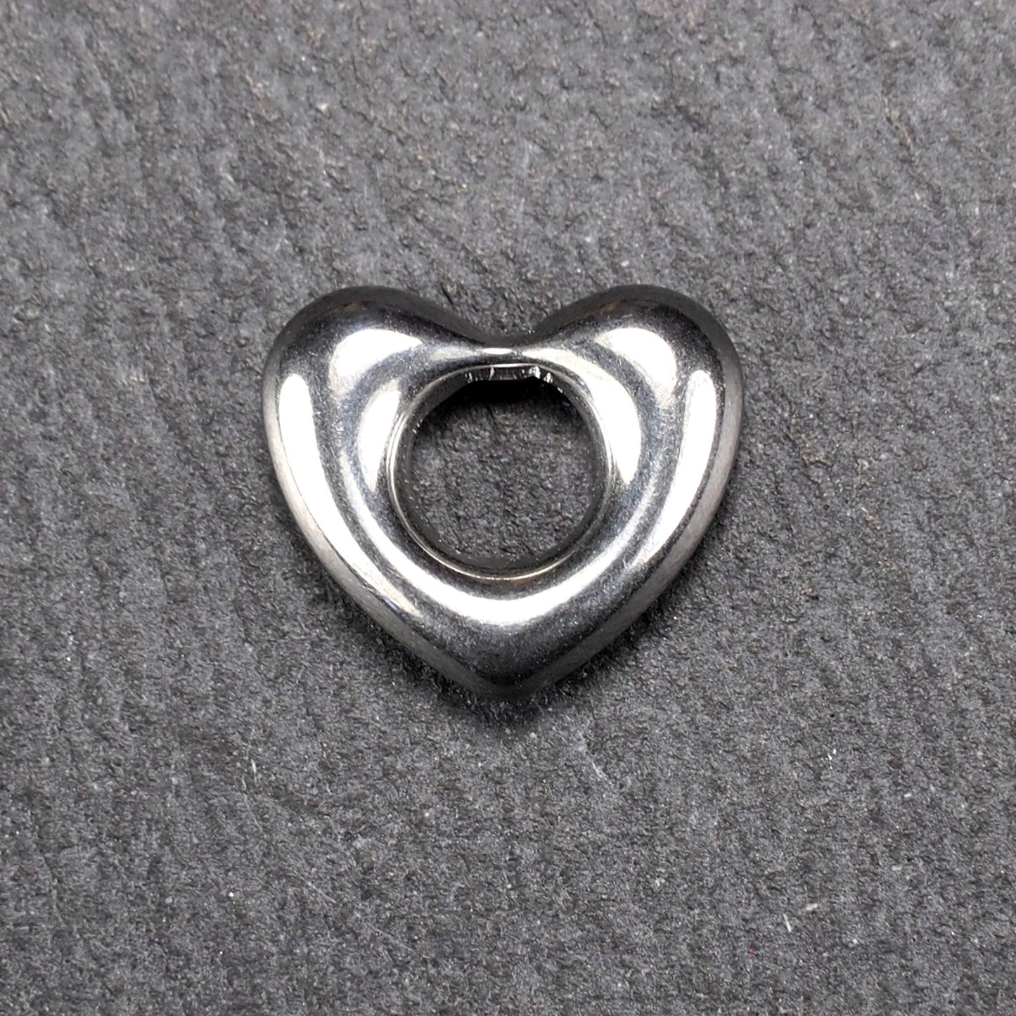 Herzanhänger, glänzend poliertes silbernes Metall mit rundem, durchbrochenem Innenfeld und glatten, abgerundeten Kanten auf dunklem Hintergrund.