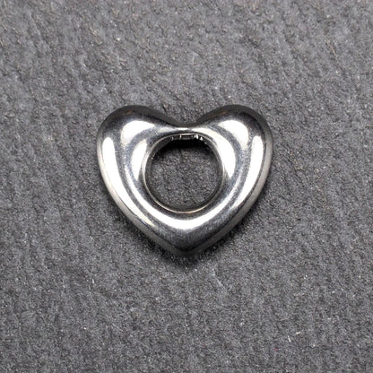 Herzanhänger, glänzend poliertes silbernes Metall mit rundem, durchbrochenem Innenfeld und glatten, abgerundeten Kanten auf dunklem Hintergrund.