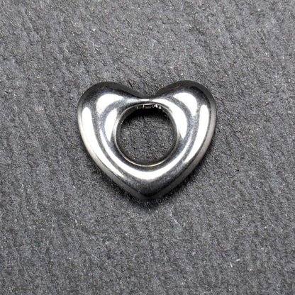 Herzanhänger, glänzend poliertes silbernes Metall mit rundem, durchbrochenem Innenfeld und glatten, abgerundeten Kanten auf dunklem Hintergrund.