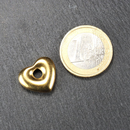 Goldfarbener, polierter Herzanhänger mit runder offener Mittelöffnung und abgerundeten Konturen, neben einer Ein-Euro-Münze als Maßstab.