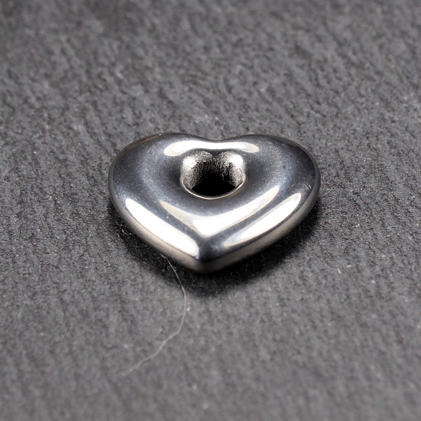 Herzförmiger, silberfarben glänzender Metallanhänger mit glatter Oberfläche und mittigem rundem Fädelloch.